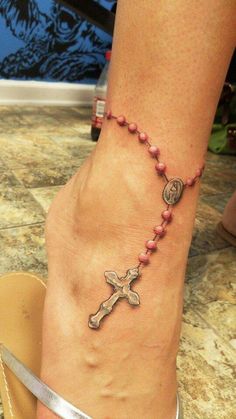 a woman's foot with a rosary on it and a cross tattoo on the ankle