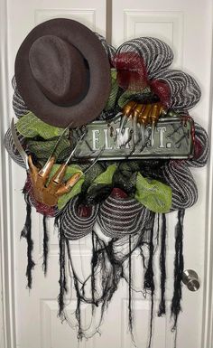 a wreath with hats, gloves and other items hanging on the front door for halloween