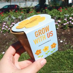 someone is holding up a box that says grow with us in front of some flowers