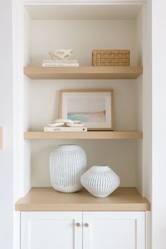 two white vases sitting on top of a wooden shelf next to a bookcase