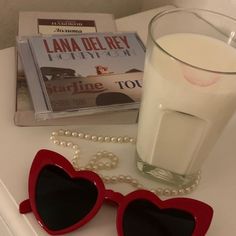 a pair of heart shaped sunglasses sitting next to a glass of milk and a book