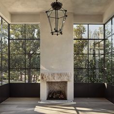 an empty room with large windows and a fire place in the center is lit by a chandelier