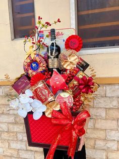 a person holding a large red basket filled with wine and chocolates in front of a brick wall