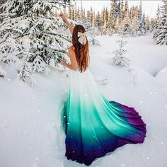 a woman standing in the snow wearing a long dress with blue and green ombrella