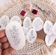 someone is holding several embroidered stones on a table with scissors and thread in the background