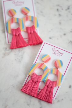 two pairs of pink and yellow tasseled earrings on top of a white card