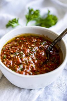 a white bowl filled with sauce and garnished with parsley on the side