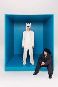 two people in white suits and black shoes are sitting in a blue box with one person dressed as a cat