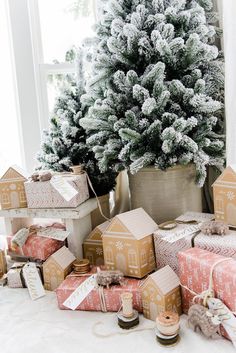 christmas presents are stacked next to a small tree in front of a window with snow on the windowsill