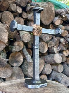 a metal cross sitting on top of a piece of wood next to some cut logs