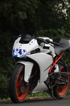 a white and orange motorcycle is parked on the side of the road with trees in the background