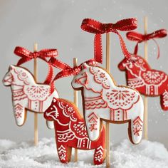 decorated cookies on sticks in the snow with red bows and ribbons hanging from it's ends