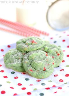 green cookies with sprinkles are on a white and red napkin next to a glass of milk