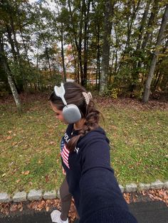 a woman with headphones on walking down the street in front of trees and grass