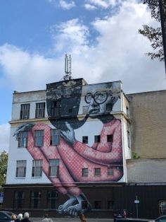 a large mural on the side of a building with people walking by and cars parked in front