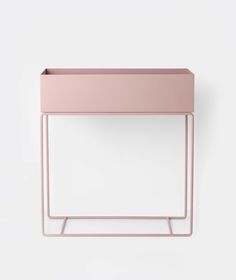 a pink planter sitting on top of a white wall next to a metal stand