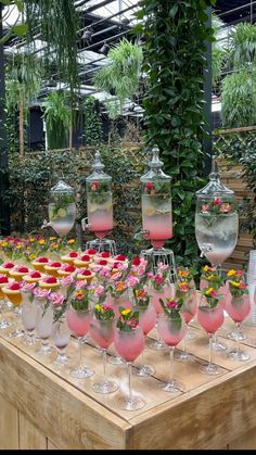 a table topped with lots of wine glasses filled with pink liquid and flowers in vases