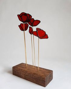 four red flowers are on sticks in a wooden holder with wood base and white background