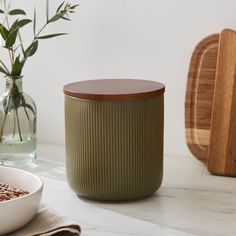 a green container sitting on top of a white counter next to a bowl and vase