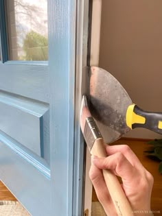 a person holding a hammer near a blue door with a wooden handle and window frame