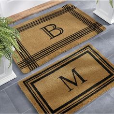 two door mats with the letter b and m on them in front of a potted plant