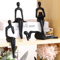 three black figurines sitting on top of a book shelf with flowers in the background