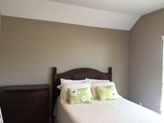 a bed with white sheets and pillows in a bedroom next to a wooden dresser under a window