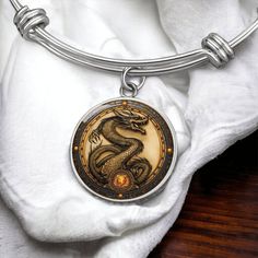 "Year of The Dragon Bracelet, a standout piece in Chinese Zodiac Animal Jewelry, serves as a symbolic Gift and Spirit Companion, featuring an Engraved Charm Pendant to celebrate the Lunar New Year 2024, embodying the strength and wisdom of the dragon. ➜ Our Dragon Jewelry is Not 3D, it's made of high quality surgical steel with a graphic image that's printed directly onto the steel surface with a shatterproof liquid glass coating and includes an 18k gold finish option. ➜ Our Engraved Dragon Pend Symbolic Zodiac Sign Collectible Jewelry, Zodiac Sign Bracelet Jewelry Gift, Symbolic Zodiac Sign Jewelry, Collectible Round Zodiac Sign Jewelry, Round Zodiac Sign Jewelry Collectible, Symbolic Metal Bracelets, Symbolic Round Metal Bracelet, Symbolic Stainless Steel Bracelet For Gifts, Symbolic Zodiac Sign Bracelet Jewelry