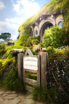 the hobbot house is surrounded by lush green plants and flowers, with a sign in front