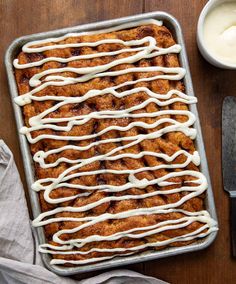 a pan filled with cinnamon rolls covered in icing next to a knife and fork