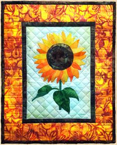 a quilted sunflower with green leaves in the center on an orange and yellow background