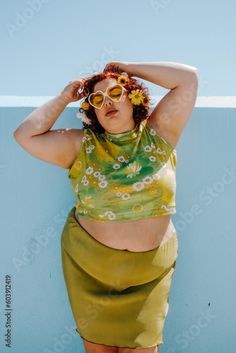 a woman in a yellow top and green skirt posing for the camera with her hands on her head