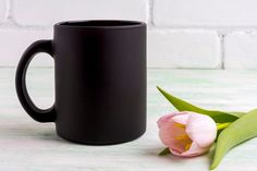 a black coffee mug sitting next to a pink tulip