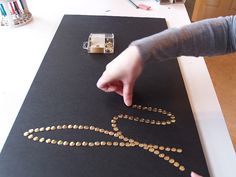 a person is making a necklace out of gold coins on a black paper with a machine in the background