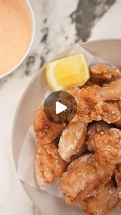 fried food on a plate with dipping sauce and lemon wedges next to the bowl