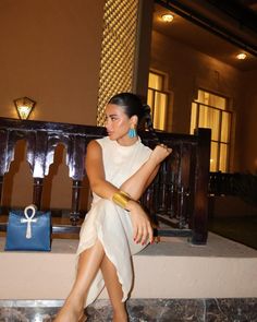 a woman sitting on a bench in front of a building with a blue purse next to her