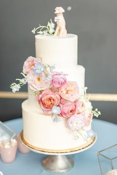 a white wedding cake with pink and blue flowers on the top tier is sitting on a table