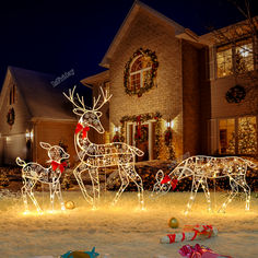 lighted reindeers in front of a house with presents on the ground and christmas lights