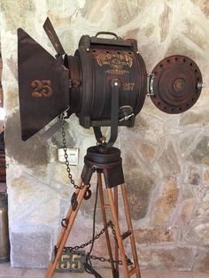 an old fashioned movie camera on a tripod in front of a stone wall with chains hanging from it