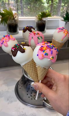 a hand holding an ice cream cone with sprinkles and chocolate on top