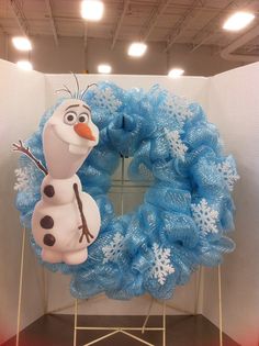 a frozen queen wreath is displayed in front of a white wall with lights on it