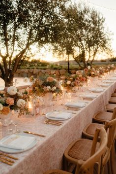 a long table is set with white plates and place settings for an outdoor dinner party