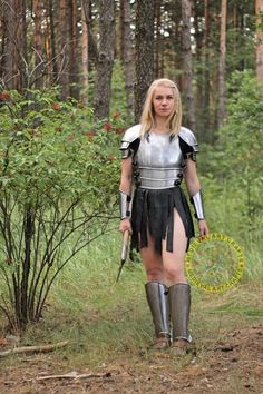 a woman dressed in armor walking through the woods