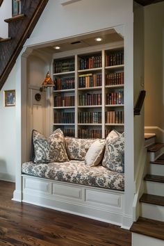 a couch sitting under a stair case next to a bookshelf filled with books