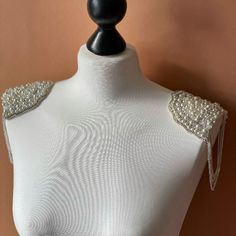 a white mannequin with pearls on it's chest and shoulder, against a brown wall