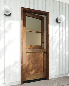 a wooden door sitting next to a white wall with two lights on it's sides