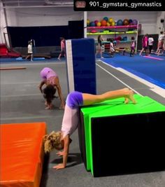 a woman doing a handstand on top of a box in an indoor gym