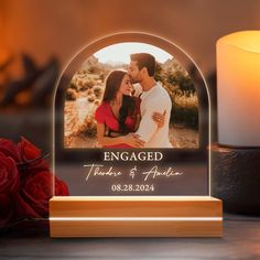 a personalized photo on a wooden stand next to a candle and some red roses