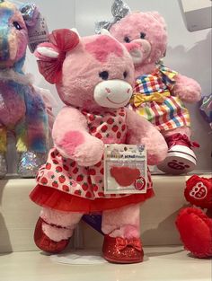 two pink teddy bears sitting next to each other in front of stuffed animals on display