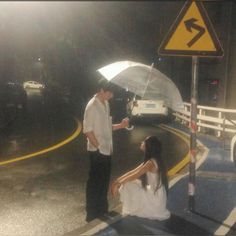 a man holding an umbrella next to a woman on the side of a road at night